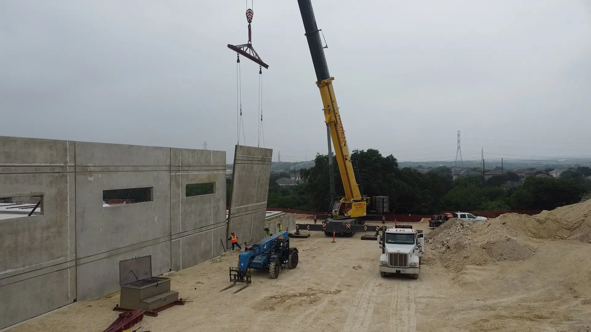 Crane lifting concrete wall panel at construction site.
